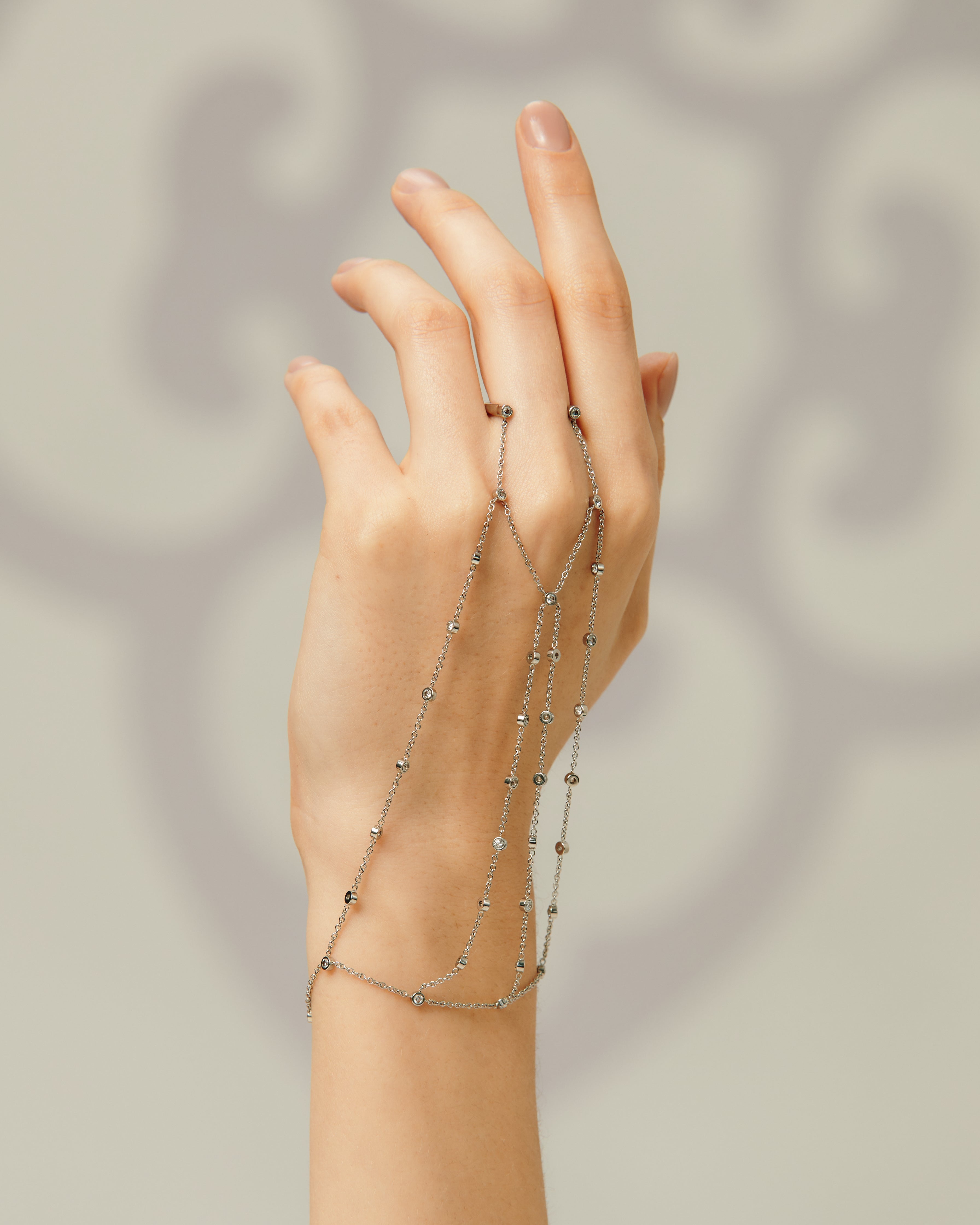 Hand wearing a delicate chain bracelet on a neutral background